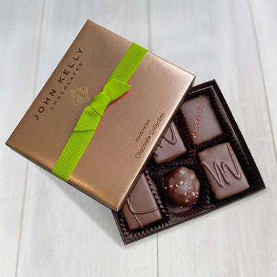 An open six piece assortment. Various chocolates from the assortment can be seen. The lid sits partially on the box and has a lime stretch ribbon.
