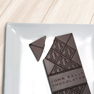 A dark solid bar with the top left corner cut off from it. The bar has a John Kelly Chocolates logo on it.