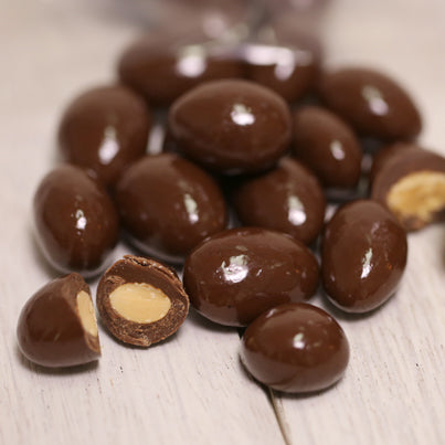 A handful of milk chocolate covered almonds sits. some are cut in half.