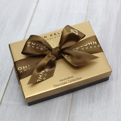 A closed salted caramel gift box. The lid is gold and features a brown ribbon that has a John Kelly Chocolates logo on it.