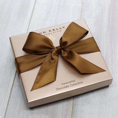 A closed 12 piece assortment. The light brown box lid has a brown ribbon on it.