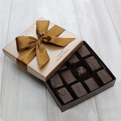 An open 12 piece assortment. Various chocolates can be seen. The lid of the box is partially on the box and features a brown ribbon.