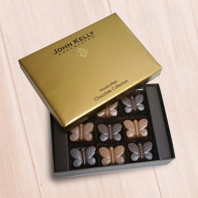 An open nine piece butterfly box with both dark and milk chocolate butterflies. The lid of the box is gold and is partially on the box.