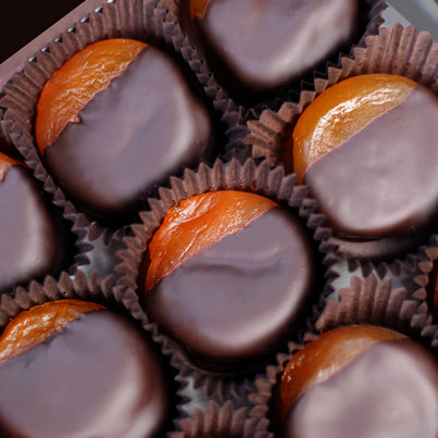 A close up picture of the chocolate dipped apricots sitting in their brown, paper cups. The apricots are covered in chocolate, but the top fourth of the apricots can be seen.