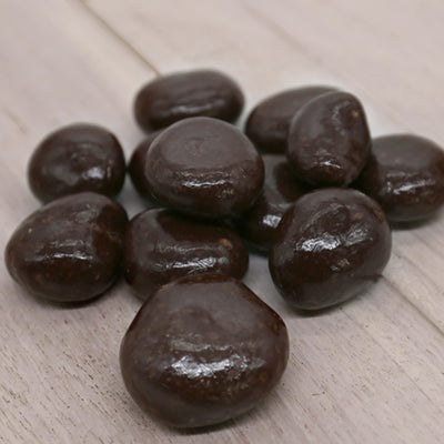 A pile of dark chocolate covered cherries sits on a wood background.