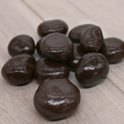 A pile of dark chocolate covered cherries sits on a wood background.