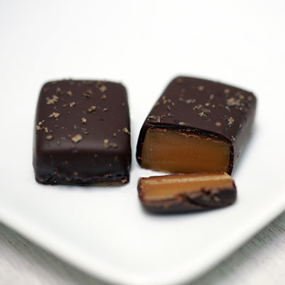 Two applewood smoked salted caramels sit on a white, square plate.