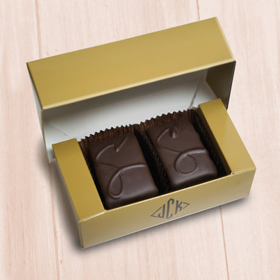A gold box sits open with two coconut truffle fudge chocolates. They each have a CO on them to signify they are coconut.