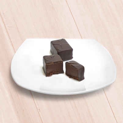 Two pieces of chocolate on a small, white, plate. The piece on the left is cut to relieve the chocolate inside it.