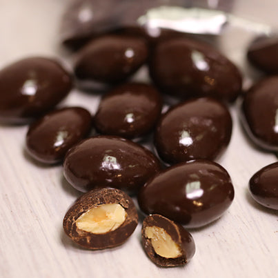 A handful of dark chocolate covered almonds is spilled on the table. Some of them are cut in half.