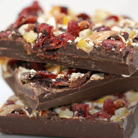 Three bars of the dark chocolate bark stacked vertically. They are topped with bits of orange and cranberry,