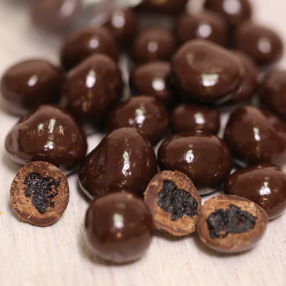 A handful of dark chocolate covered blueberries all over a table. A few in the front are cut in half.