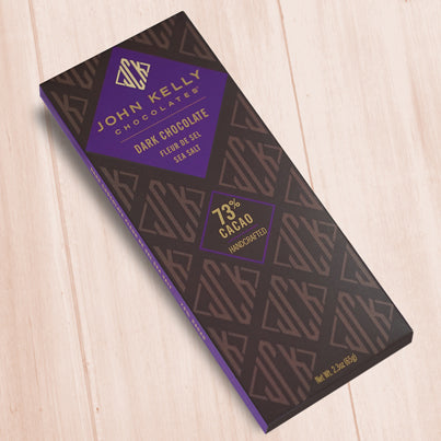 A dark brown, rectangular box. There is a purple diamond on it that holds a John Kelly Chocolates logo and the product name.