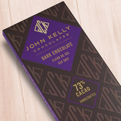 A dark brown, rectangular box. There is a purple diamond on it that holds a John Kelly Chocolates logo and the product name.