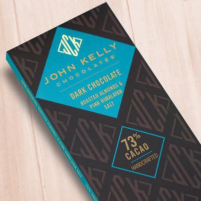 A dark brown, rectangular box. There is a light blue diamond on it that holds a John Kelly Chocolates logo and the product name.