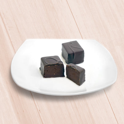 Two chocolate bars sit on a white, square plate. One is cut.