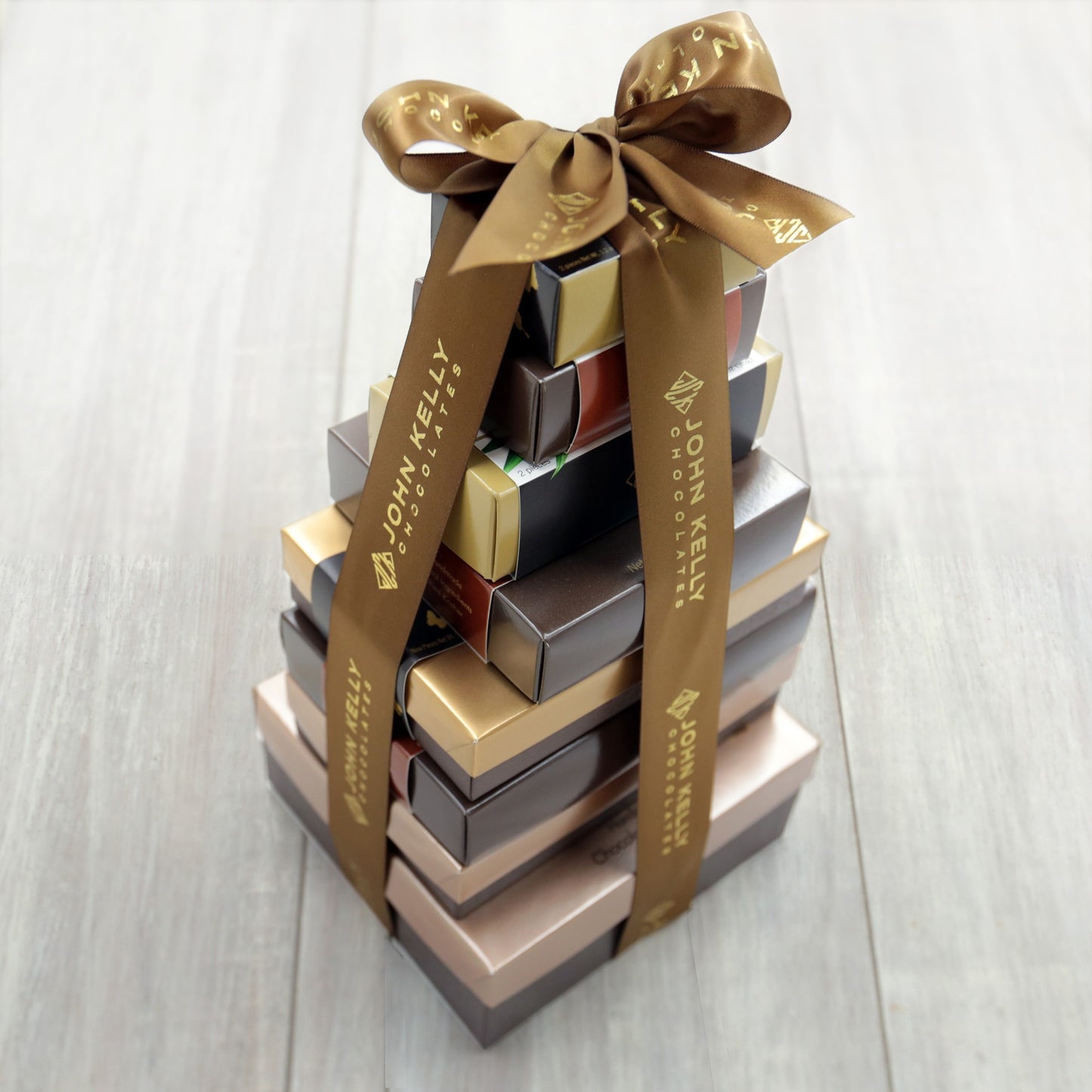 Eight boxes stacked vertically from largest to smallest. They are held together with a brown bow that has John Kelly Chocolates written on it.