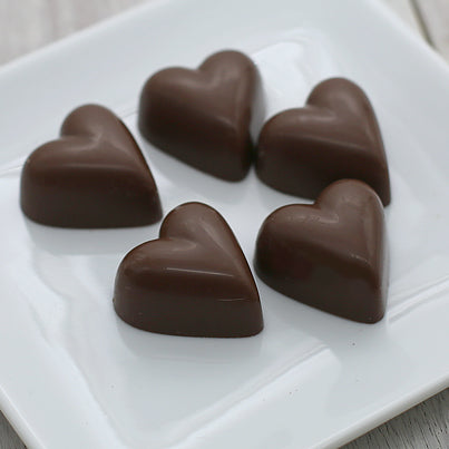 Six milk chocolate hearts are placed on a white square plate.