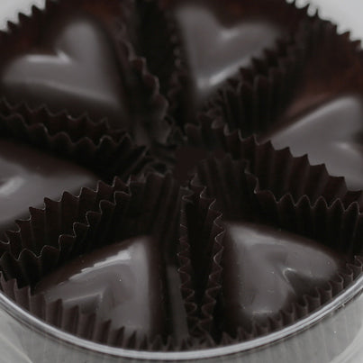 Six dark chocolate hearts sit in an open container.