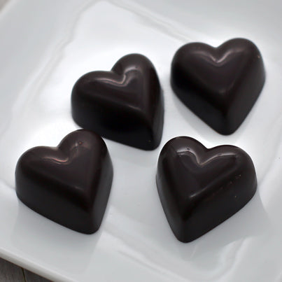 Four dark chocolate hearts sit on a white, square plate.