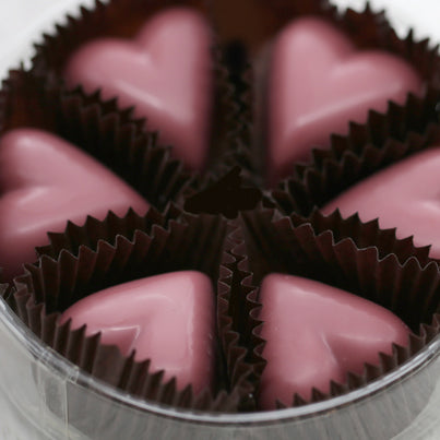 Six pink ruby chocolate hearts in an open container. All of the hearts are in brown, paper, cups.