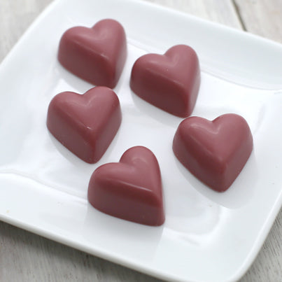 Five pink ruby chocolates sit on a white, square plate