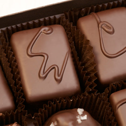 A close up of a chocolate piece with a CW on it to signify it is semi-sweet with walnuts.