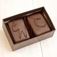 An open two piece assortment. Two chocolates with C and CW labeled on them sit neatly in the box.