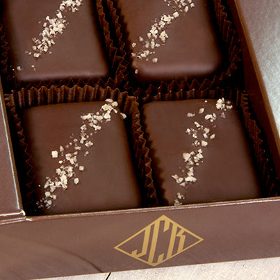 A close up of an open dark brown box containing four grey salted truffle fudge bites.