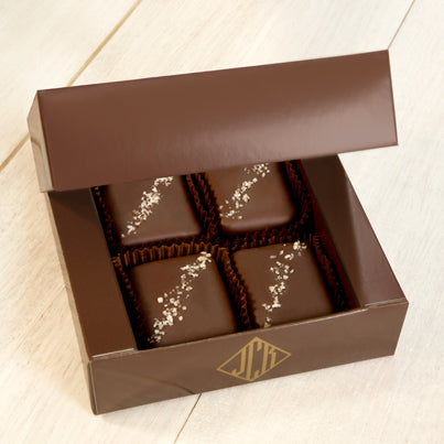 An open dark brown box containing four grey salted truffle fudge bites.