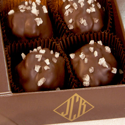 Four walnut caramel clusters in an open box. The box is a dark brown.