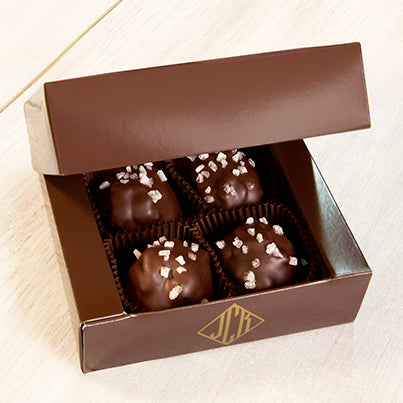 Four walnut caramel clusters in an open box. The box is a dark brown.
