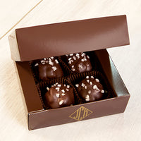 Four walnut caramel clusters in an open box. The box is a dark brown.