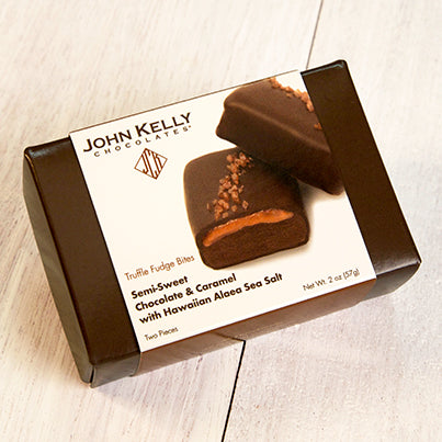 A dark brown box with a white sleeve on it. The sleeve features an image of two red salted truffle fudge bites.