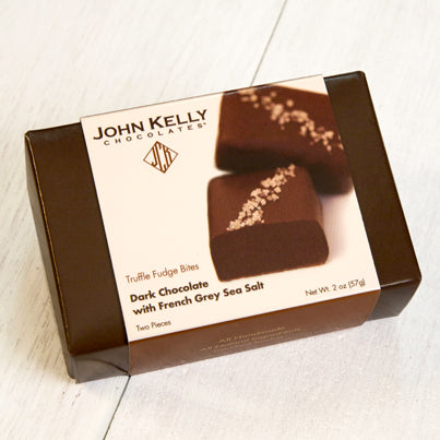 A dark brown box with a white sleeve. The sleeve features a photo of two salted truffle fudge bites on it as well as a brown John Kelly Chocolates logo.
