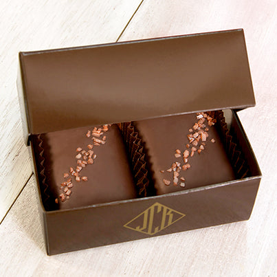 Two red salted chocolates sit in a dark brown box.