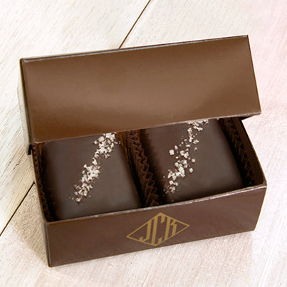 Two grey salted truffle fudge bites in a dark brown box.