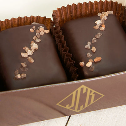 A close up of two pink salted truffle fudge bites in a dark brown box.