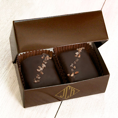 An open dark brown box with two pink salted truffle fudge bites inside.