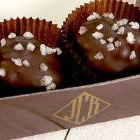 Two salted walnut clusters in brown, paper cups. The cups are sitting in a dark brown box.
