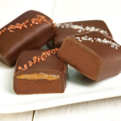 Four salted truffle fudge bites sit on a plate. Two of then have a red colored salt and the other two have a grey salt.