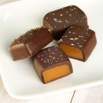 Four fleur de sel salted caramels on a plate. Two in the front are sliced to reveal the gooey caramel inside.