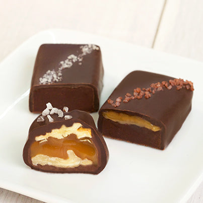 Two salted fudge bites and walnut caramel cluster sit on a white plate.