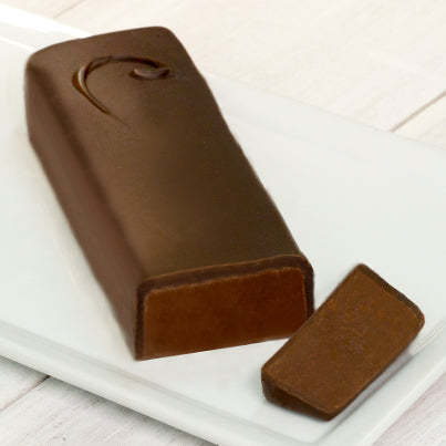A long chocolate bar with a C on it to signify it is the semi-sweet chocolate bar. A sliver of the end of the bar is cut off to reveal the chocolate inside.