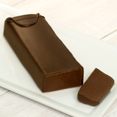 A long rectangular chocolate bar with a D on it to signify it is a dark chocolate bar. A sliver of the end of the bar is cut to reveal the chocolate inside.