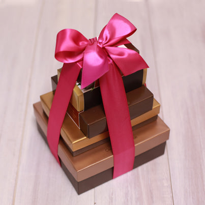 Five boxes stacked vertically from largest to smallest. They are tied together with a fuchsia ribbon.
