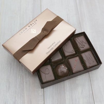 An open eight piece assortment. Various chocolates from the assortment can be seen. The lid is partially on the box. The lid is light brown and has a brown ribbon on it.