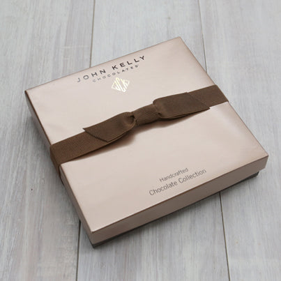 A closed 12 piece assortment. The lid is light brown and includes a brown stretch ribbon.