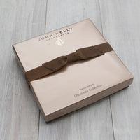 A closed 12 piece assortment. The lid is light brown and includes a brown stretch ribbon.