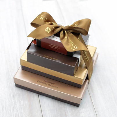 Four boxes stacked vertically from largest to smallest. They are tied together with a brown bow that reads John Kelly Chocolates.